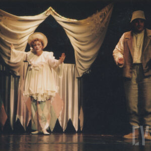 teatrzyk lalkowy utworzony z tkaniny, przed nim aktorka w kostiumie klauna, z prawej aktor w kostiumie