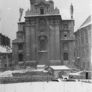 uszkodzona elewacja budynku kościelnego z oknami, blendami i pilastrami, przed elewacją zagruzowany plac