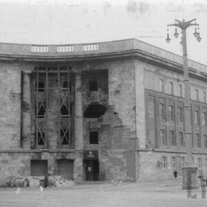 duży, dwuskrzydłowy budynek z owalną wnęką na narożniku ze znacznymi ubytkami w elewacji