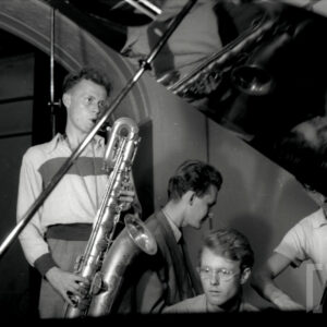 młody mężczyzna grający na saksofonie i drugi siedzący przy pianinie w studio nagraniowym