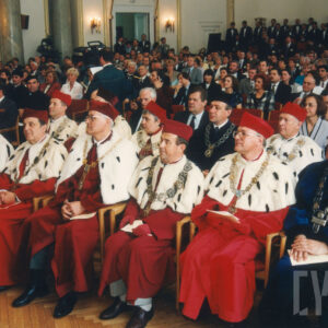 elegancko ubrani ludzie w różnym wieku, siedzący na krzesłach, w pierwszych dwóch rzędach kobiety i mężczyźni w togach władz uczelnianych 