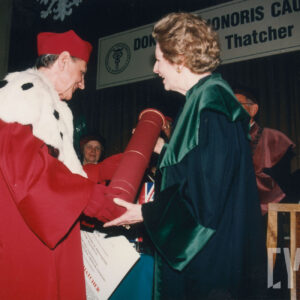 starszy mężczyzna i starsza kobieta, ubrani w togi uniwersyteckie, mężczyzna wręcza kobiecie tubę