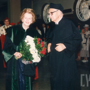 starsza kobieta ubrana w togę, w towarzystwie starszego mężczyzny w okularach i todze