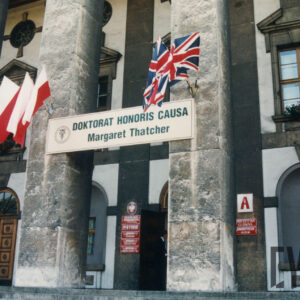 monumentalny budynek z kamienia; filary przyozdobione banerem z informacją o odbywającej się uroczystości oraz flagami Wielkiej Brytanii i Polski