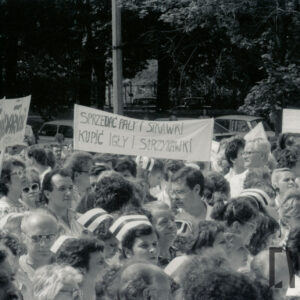 duża grupa kobiet, między nimi kilku mężczyzn, większość w białych kitlach, część kobiet ma na głowach pielęgniarskie czepki, część trzyma nad głowami transparenty z hasłami