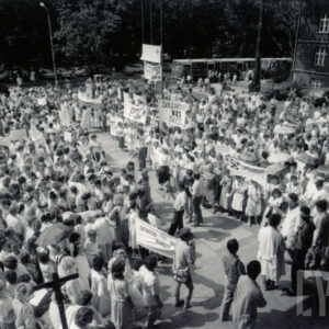 tłum ludzi na placu, większość w białych kitlach, część trzyma transparenty z hasłami