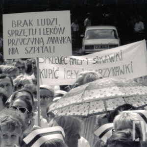 grupa ludzi, widoczne właściwe tylko ich głowy, kilka kobiet w czepkach pielęgniarskich, nad głowami transparenty z hasłami