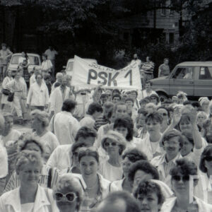 tłum ludzi, w większości w białych kitlach, nad głowami transparent