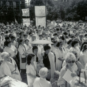 tłum ludzi, przeważnie w białych kitlach, stoi na placu, większość kobiety