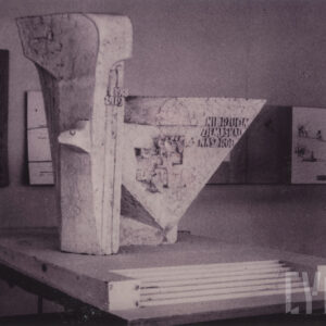 dwie połączone z sobą gipsowe bryły, jedna pionowa, druga trójkątna, stojąca na jednym z kątów, całość umieszczona na schodkowym postumencie