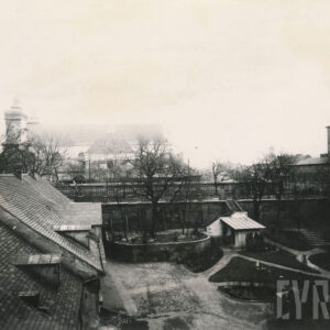 duża niezbyt zabudowana przestrzeń z niewielkimi budynkami gospodarczymi, ogrodem i brukowanym podwórzem, w tle, ponad drzewami bez liści, widoczne zarysy budynków