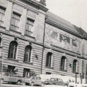 monumentalny, klasycystyczny z dekoracyjną elewacją; przed budynkiem widoczne samochody, a na chodniku przechodnie