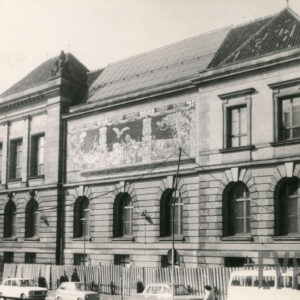 monumentalny, klasycystyczny z dekoracyjną elewacją; przed budynkiem widoczne samochody, a na chodniku przechodnie