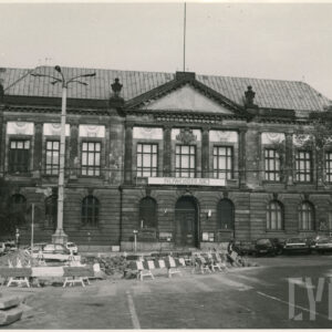 monumentalny, klasycystyczny budynek z kolumnowym wejściem i dekoracyjnym frontonem; przed budynkiem stoją samochody; widoczne też roboty drogowe