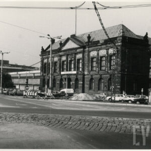 monumentalny, klasycystyczny budynek z kolumnowym wejściem i dekoracyjnym frontonem; przed budynkiem stoją samochody; widoczne też roboty drogowe