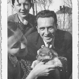 młoda dziewczyna z małym pieskiem na rękach, nad nią młody chłopiec, obok niej roześmiany mężczyzna