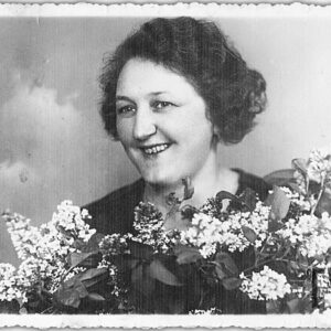 zdjęcie portretowe uśmiechniętej kobiety w średnim wieku przysłoniętej bukietem bzu