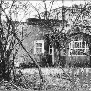 parterowy dom z werandą z oknami z gęstymi szprosami przysłonięty pozbawionymi liści gałęziami drzew