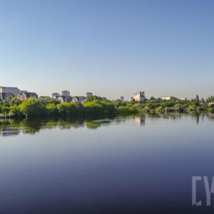 rzeka o wyraźnie podniesionym stanie, wzdłuż jej brzegów zielone, bujne drzewa oraz budynku