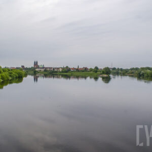 rzeka o wyraźnie podniesionym stanie, wzdłuż jej brzegów zielone, bujne drzewa oraz budynku