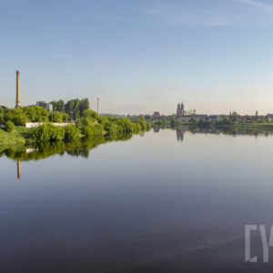 rzeka o wyraźnie podniesionym stanie, wzdłuż jej brzegów zielone, bujne drzewa oraz budynku