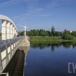 most łączący dwa brzegi, pod nim rzeka o wyraźnie podniesionym stanie; w głębi zarysy budynków