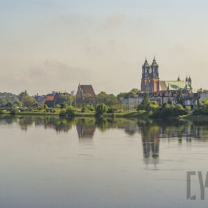rzeka o wyraźnie podniesionym stanie, wzdłuż jej brzegów zielone, bujne drzewa oraz budynku
