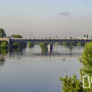 rzeka o wyraźnie podniesionym stanie, wzdłuż jej brzegów zielone, bujne drzewa oraz budynku