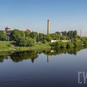 rzeka o wyraźnie podniesionym stanie, wzdłuż jej brzegów zielone, bujne drzewa oraz budynku