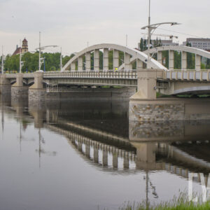 most łączący dwa brzegi, pod nim rzeka o wyraźnie podniesionym stanie; w głębi zarysy budynków