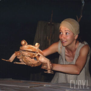 kobieta trzyma w wyciągniętych rękach drewnianą lalkę żaby