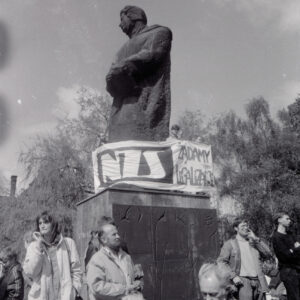 duży pomnik mężczyzny, na cokole stoją mężczyźni trzymając w rękach transparent, pod pomnikiem ludzie