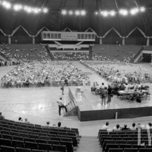 duża okrągła hala, pośrodku siedzą ludzie, na podwyższeniu stół, przy nim siedzi kilka osób