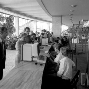 półokrągły hol, pośrodku lada, za nią, z prawej puste wieszaki, przy ladzie stoją ludzie