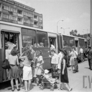 wsiadający do autobusu ludzie, w głębi fragment bloku mieszkalnego