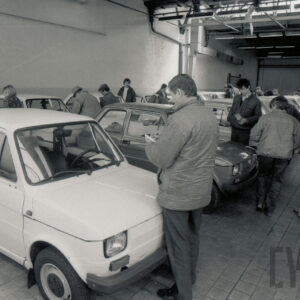 duża hala, w niej ludzie oglądający zaparkowane w rzędach samochody osobowe