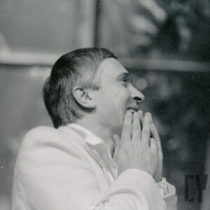 mężczyzna ujęty do piersi stoi bokiem ze złożonymi jak do modlitwy dłońmi