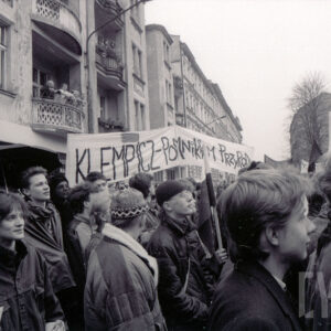 duże zgromadzenie młodych osób z transparentami, w głębi kilkupiętrowe kamienice