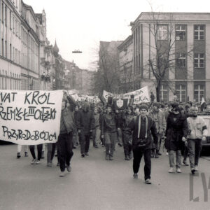 przemarsz ulicą młodych osób z transparentami, w głębi budynki