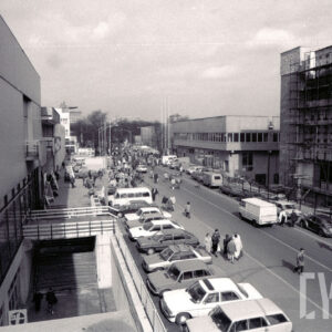 aleja na terenie targów, po obu stronach pawilony wystawiennicze, z prawej pawilon w trakcie remontu, otoczony rusztowaniami, po obu stronach alei zaparkowane samochody, pomiędzy nimi chodzą ludzie