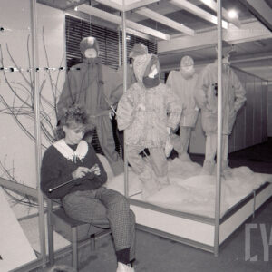 hala ze stoiskami z manekinami, na których prezentowana jest odzież, przed stoiskiem na krześle siedzi młoda kobieta i robi na drutach