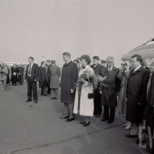 duża grupa ludzi zgromadzona na płycie lotniska, w środku kobieta i mężczyzna, w głębi jasny budynek z wieżą i napisem Poznań