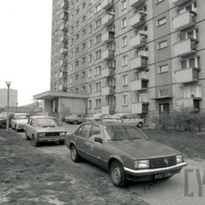 wysoki blok mieszkalny z wielkie płyty, przed nim zaparkowane samochody osobowe