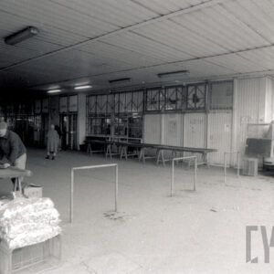 blaszany budynek handlowy, z lewej dwóch mężczyzn przy rozłożonym drewnianym stoisku, z prawej samochód dostawczy