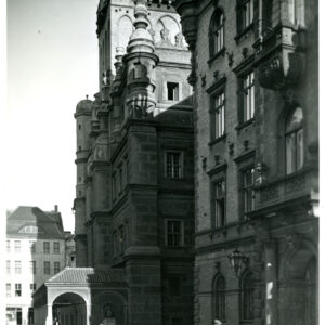 elewacje dwóch, okazałych budynków, przy ścianie budynku usytuowanego w głębi parterowa przybudówka z podcieniami, na pierwszym planie dwóch mężczyzn w mundurach