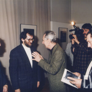 czterech mężczyzn stoi na tle zawieszonych na ścianach fotografii, dwóch prowadzi rozmowę