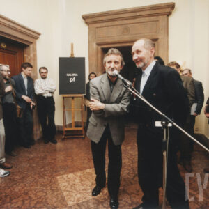 pomieszczenie z marmurową podłogą i trojgiem drzwi w okazałych obramieniach, pod ścianami stoi kilka osób, na pierwszym planie dwóch mężczyzn rozmawia przed mikrofonem