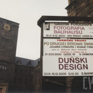 tablice informacyjne umieszczone na metalowej konstrukcji, w głębi fragment wieży i mury potężnego zamku