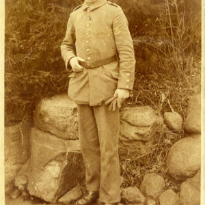 młody mężczyzna w mundurze wojskowym i czapką na głowie stoi na tle naturalnego otoczenia z kamieniami i rzadką roślinnością