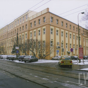 zimowa sceneria, pięciokondygnacyjny prosty budynek przy ulicy, przed nim zaparkowane samochody